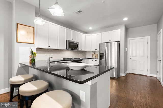 kitchen featuring visible vents, a peninsula, a sink, appliances with stainless steel finishes, and tasteful backsplash