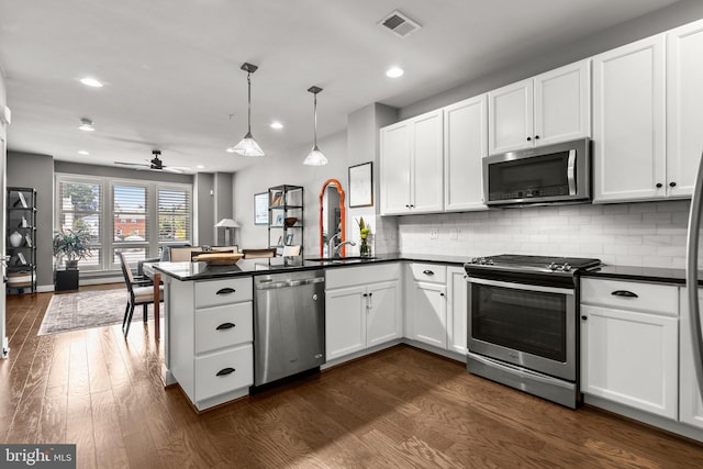 kitchen with a peninsula, dark wood-style floors, dark countertops, and appliances with stainless steel finishes