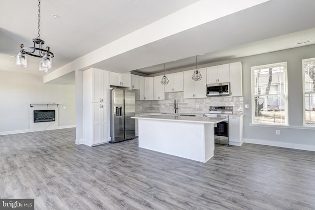 kitchen featuring light countertops, appliances with stainless steel finishes, a glass covered fireplace, open floor plan, and white cabinets