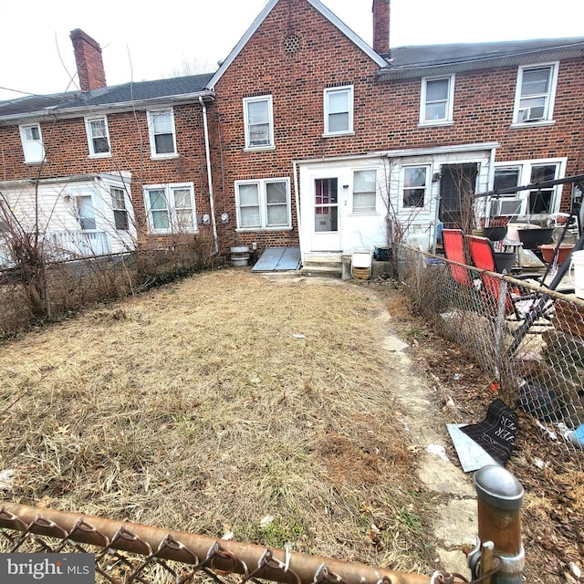 rear view of house with entry steps, brick siding, and fence