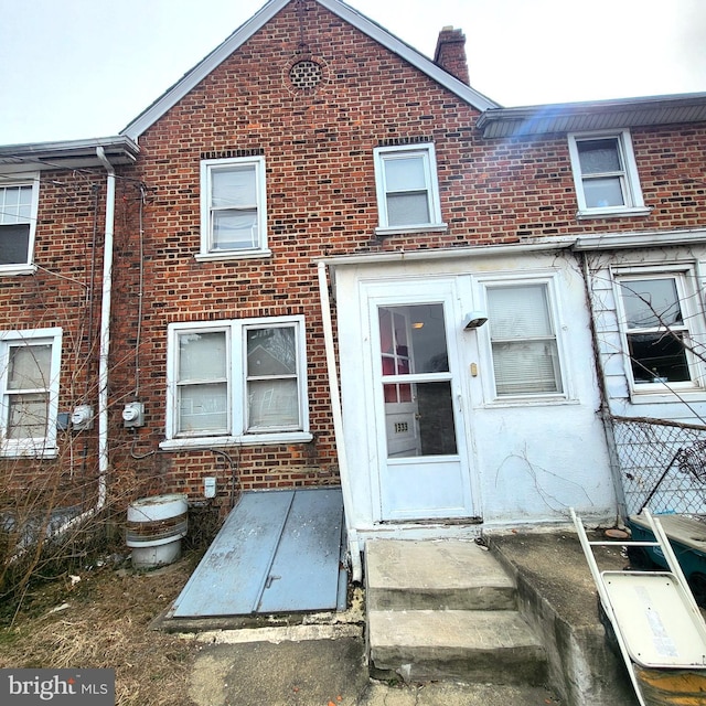 view of front of property featuring entry steps, a chimney, and brick siding