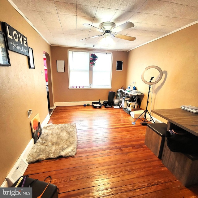 workout room featuring baseboards, arched walkways, a ceiling fan, ornamental molding, and wood finished floors