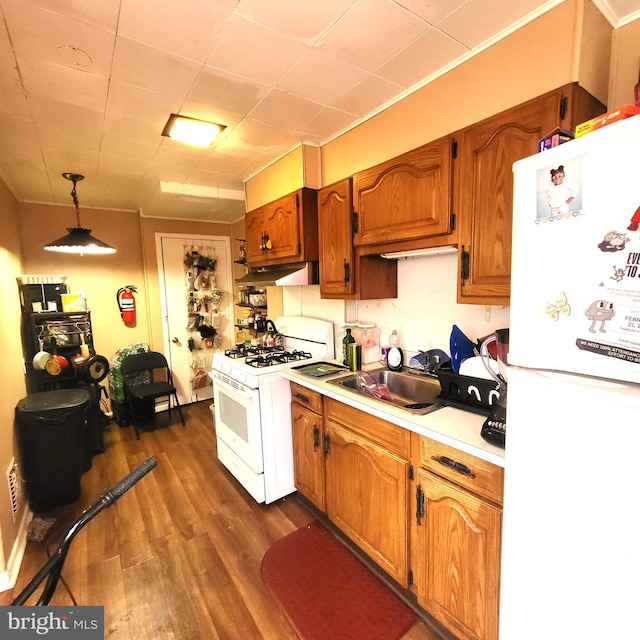 kitchen featuring white appliances, a sink, light countertops, brown cabinetry, and decorative light fixtures