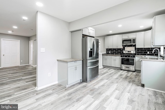 kitchen with sink, tasteful backsplash, light stone counters, light hardwood / wood-style flooring, and appliances with stainless steel finishes