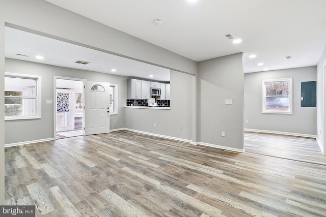 unfurnished living room with electric panel and light hardwood / wood-style flooring