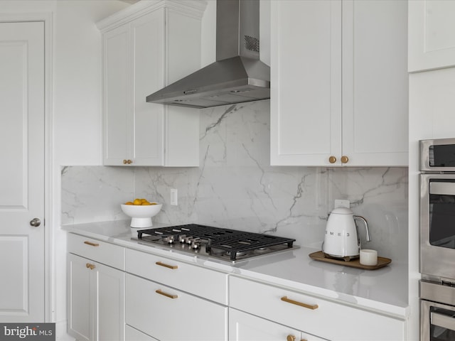 kitchen with backsplash, white cabinets, stainless steel appliances, and wall chimney range hood