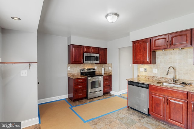 kitchen featuring reddish brown cabinets, stainless steel appliances, a sink, and baseboards