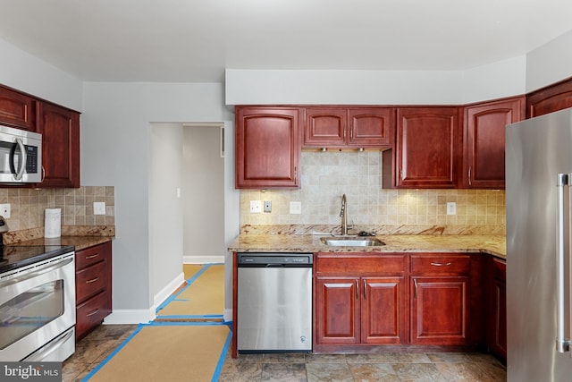 kitchen with reddish brown cabinets, light stone countertops, stainless steel appliances, and a sink