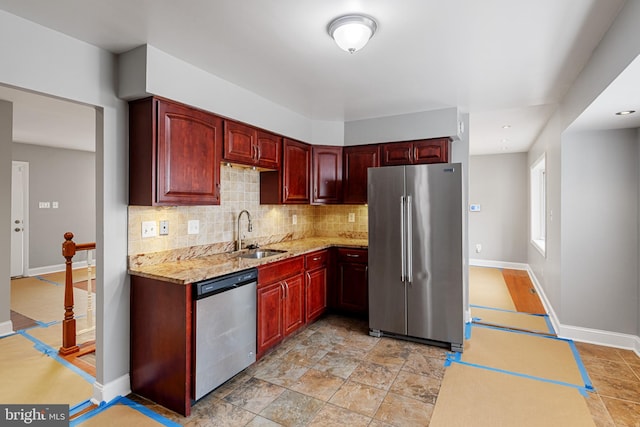 kitchen featuring reddish brown cabinets, tasteful backsplash, appliances with stainless steel finishes, light stone countertops, and a sink