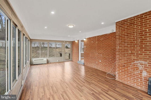 unfurnished living room featuring brick wall, ornamental molding, wood finished floors, an AC wall unit, and recessed lighting