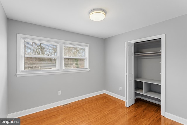 unfurnished bedroom with a closet, wood finished floors, visible vents, and baseboards