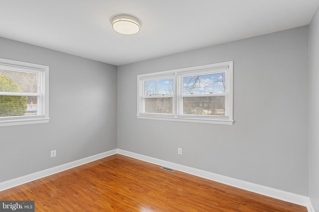 empty room with wood finished floors, visible vents, and baseboards