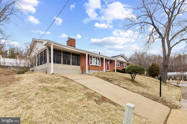 ranch-style home featuring brick siding, a sunroom, a chimney, fence, and a front yard