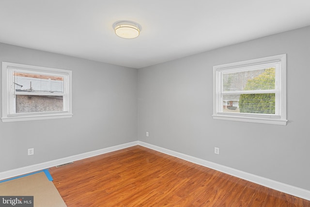 unfurnished room featuring baseboards, wood finished floors, and a healthy amount of sunlight