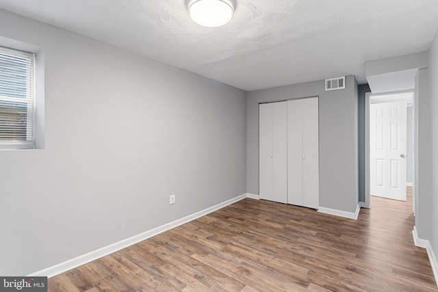 unfurnished bedroom with baseboards, a closet, visible vents, and wood finished floors