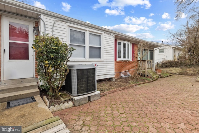 view of side of home featuring entry steps, brick siding, and central air condition unit