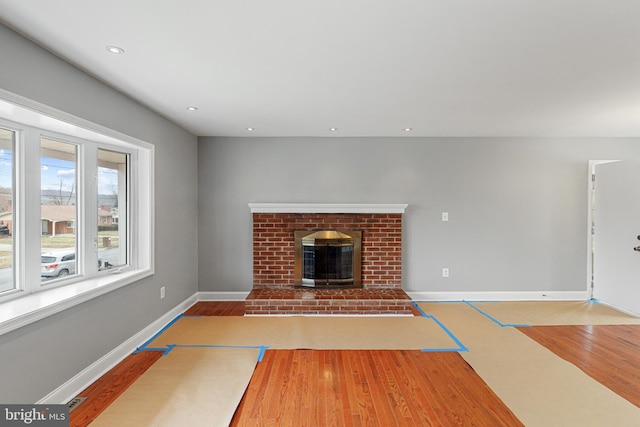 unfurnished living room with basketball hoop, recessed lighting, a brick fireplace, wood finished floors, and baseboards