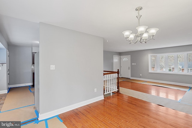 interior space with baseboards, wood finished floors, an upstairs landing, and an inviting chandelier