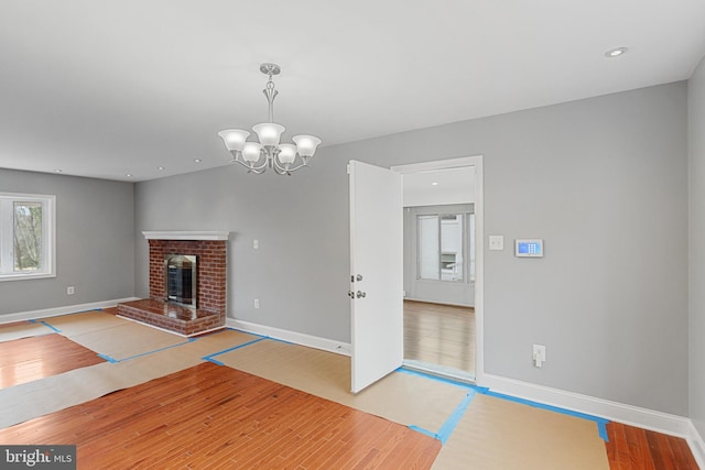 unfurnished living room with a brick fireplace, baseboards, wood finished floors, and an inviting chandelier