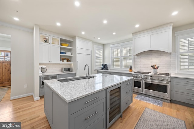 kitchen with wine cooler, sink, white cabinetry, stainless steel appliances, and a kitchen island with sink