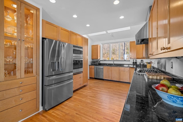 kitchen with appliances with stainless steel finishes, lofted ceiling, sink, dark stone countertops, and light hardwood / wood-style floors