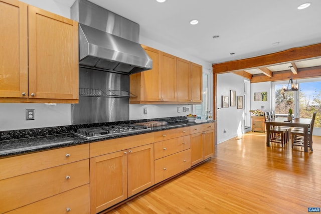 kitchen featuring pendant lighting, range hood, stainless steel gas stovetop, dark stone countertops, and light hardwood / wood-style floors