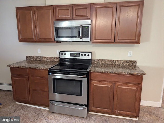 kitchen with stainless steel appliances, a baseboard heating unit, and dark stone countertops