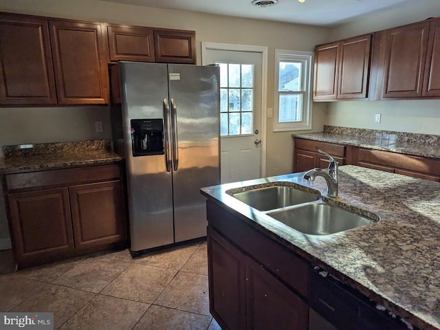 kitchen with sink, dishwasher, dark stone countertops, light tile patterned flooring, and stainless steel fridge with ice dispenser