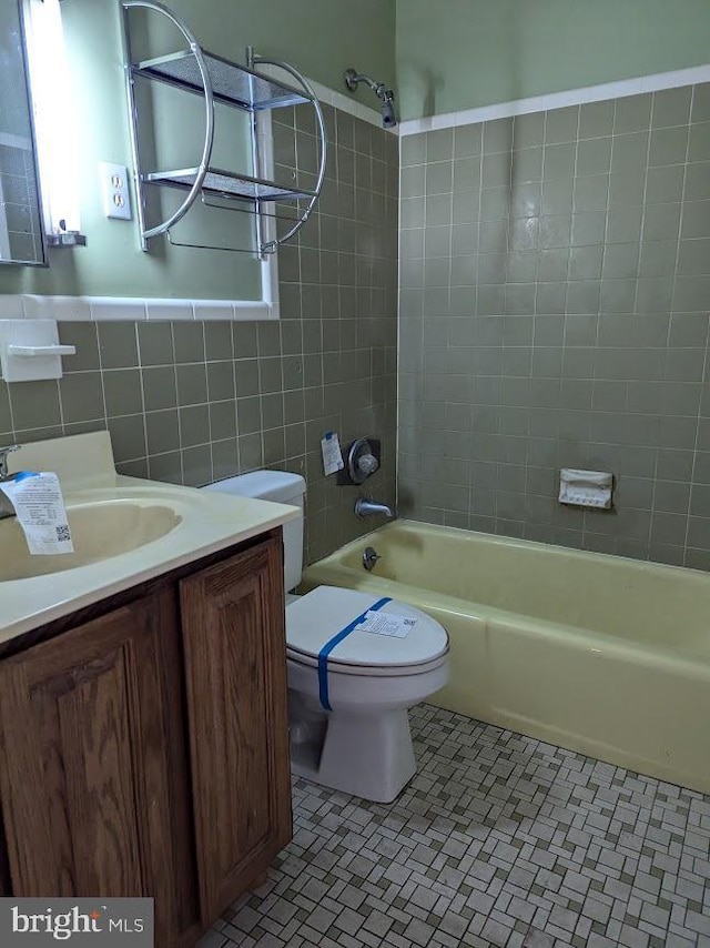 full bathroom with tile walls, tiled shower / bath combo, vanity, tile patterned floors, and toilet