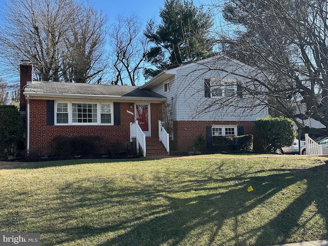 split level home with entry steps, a front yard, a chimney, and brick siding