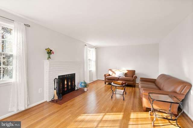 living room featuring light wood-style flooring, a brick fireplace, and baseboards