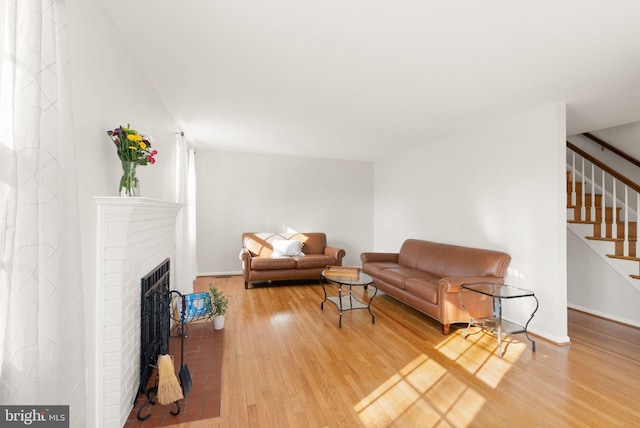 living room featuring a brick fireplace, stairs, light wood-type flooring, and baseboards