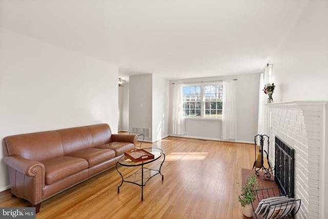 living room with visible vents, a brick fireplace, baseboards, and light wood-style floors