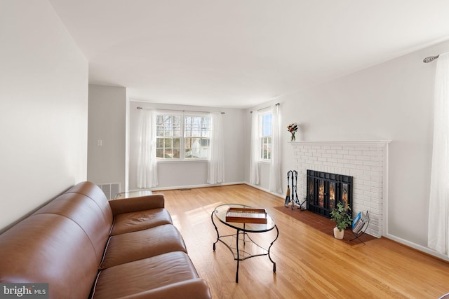 living area featuring a brick fireplace, light wood-style floors, visible vents, and baseboards