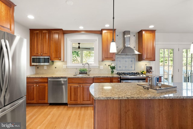 kitchen with a sink, stainless steel appliances, wall chimney exhaust hood, and brown cabinetry