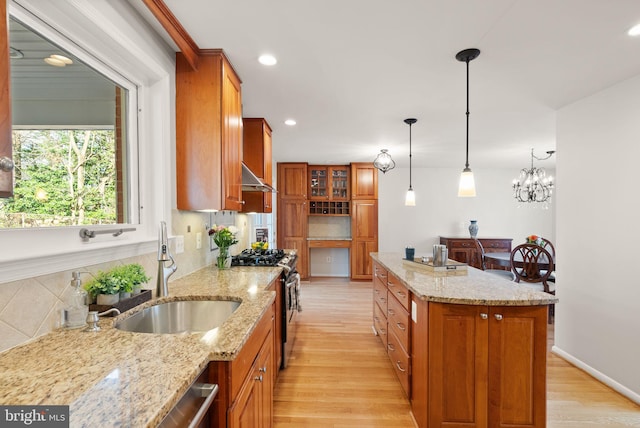 kitchen featuring stainless steel gas range oven, light wood-type flooring, brown cabinetry, and exhaust hood