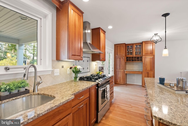 kitchen featuring a sink, stainless steel range with gas stovetop, brown cabinetry, and wall chimney range hood