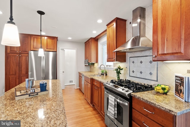 kitchen featuring light stone counters, light wood-style flooring, appliances with stainless steel finishes, wall chimney exhaust hood, and a sink