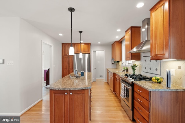 kitchen featuring light wood-style flooring, a sink, a kitchen island, appliances with stainless steel finishes, and wall chimney range hood