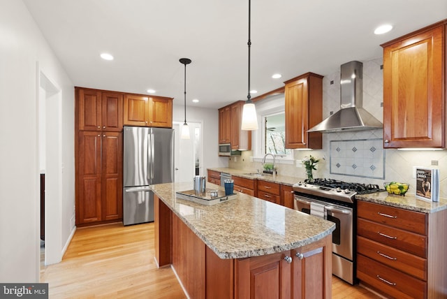 kitchen featuring light wood-type flooring, appliances with stainless steel finishes, a center island, and wall chimney exhaust hood