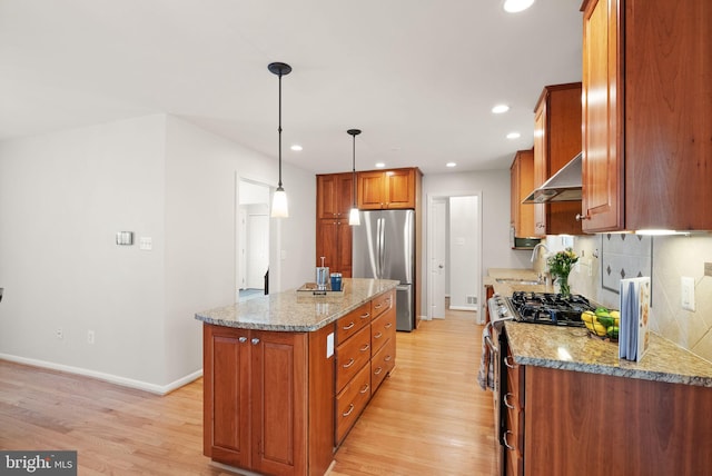 kitchen featuring under cabinet range hood, brown cabinets, light wood finished floors, and stainless steel appliances