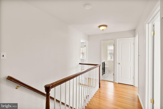 hallway with baseboards, an upstairs landing, and light wood finished floors