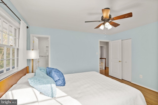 bedroom with baseboards, ensuite bath, a ceiling fan, and wood finished floors