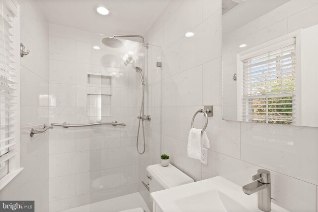 full bathroom featuring visible vents, toilet, a sink, a tile shower, and tile walls