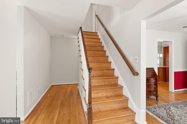 staircase featuring wood finished floors, visible vents, and baseboards