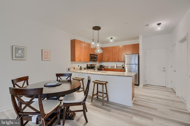 kitchen featuring sink, hanging light fixtures, light wood-type flooring, kitchen peninsula, and stainless steel appliances