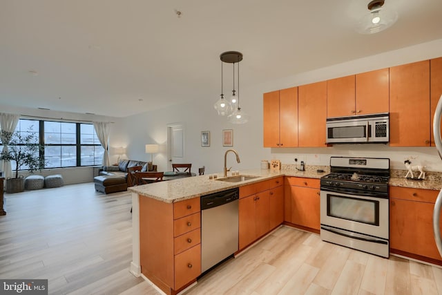 kitchen with sink, appliances with stainless steel finishes, decorative light fixtures, kitchen peninsula, and light wood-type flooring