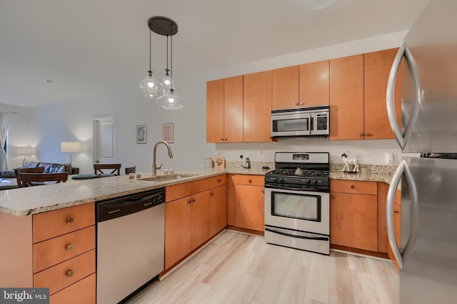 kitchen with appliances with stainless steel finishes, sink, hanging light fixtures, light hardwood / wood-style floors, and kitchen peninsula