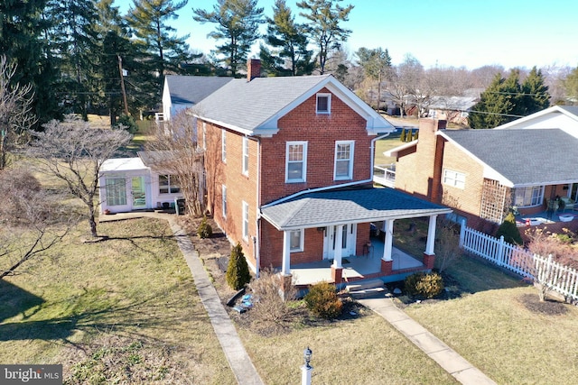 traditional-style home featuring a porch, brick siding, fence, roof with shingles, and a front yard