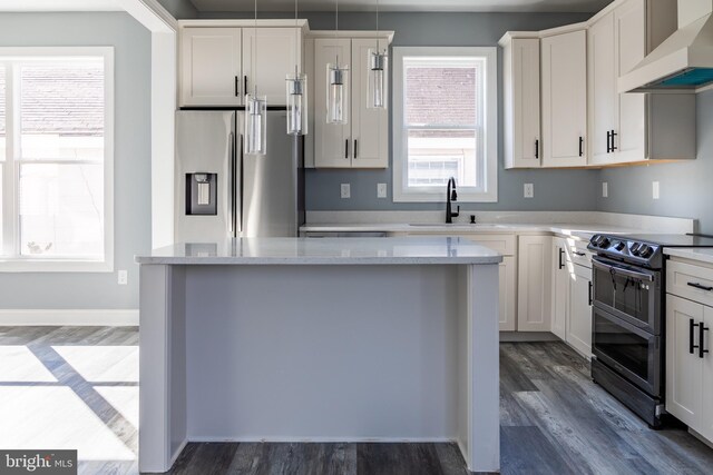 kitchen with stainless steel appliances, a sink, white cabinetry, hanging light fixtures, and wall chimney exhaust hood